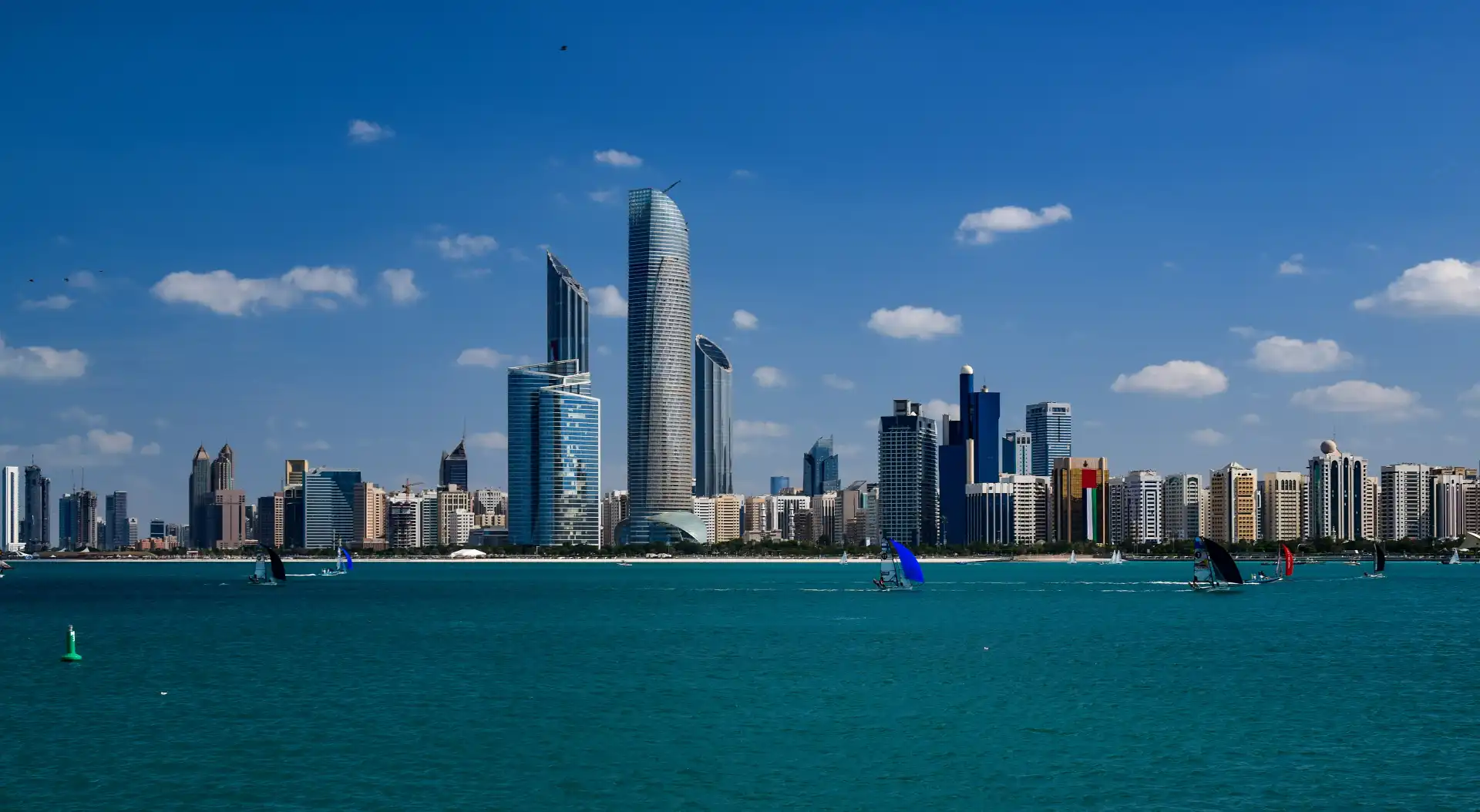 Abu Dhabi skyline with modern skyscrapers viewed across the turquoise waters of the Corniche, with sailboats racing in the foreground