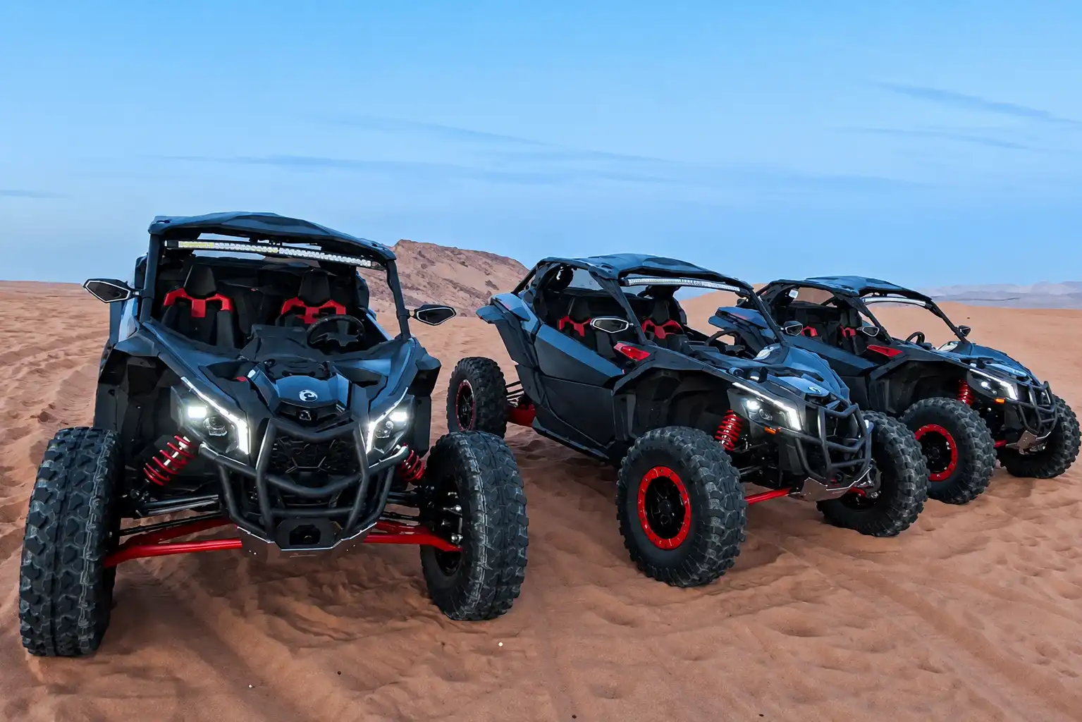 Three black off-road buggies with red accents parked in a row on a desert sand dune
