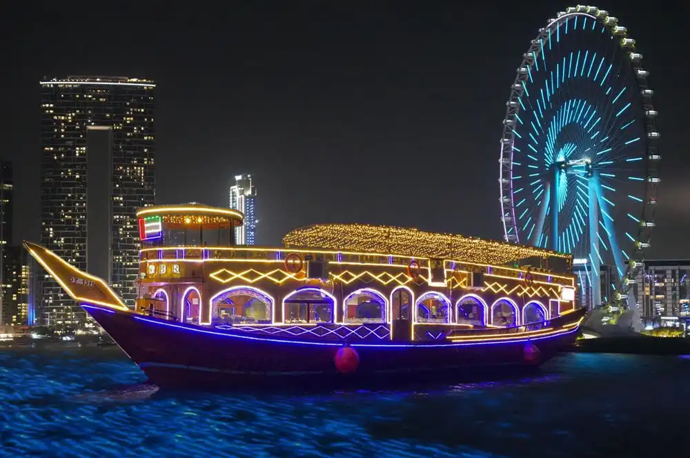 Traditional illuminated dhow cruise boat on the water at night with Ain Dubai observation wheel in the background