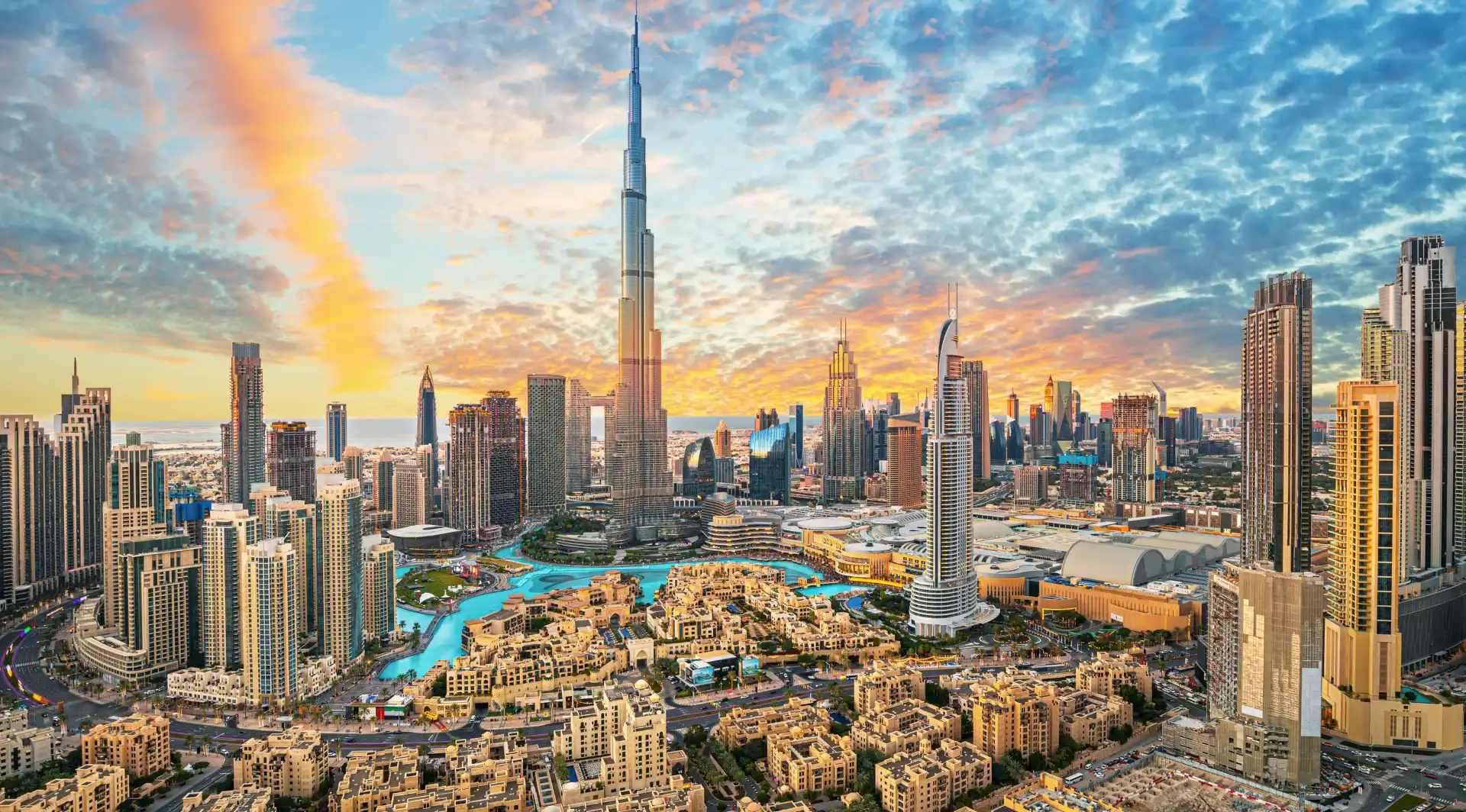 Aerial sunset view of Downtown Dubai skyline featuring Burj Khalifa, Dubai Mall, and the Burj Khalifa Lake surrounded by high-rise towers