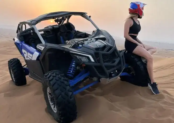 Woman wearing a helmet sitting on a blue and black off-road buggy in the Dubai desert at sunset
