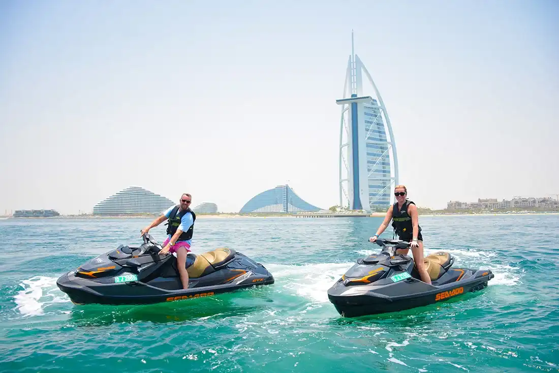 Two jet skis with riders speeding across the water in front of the Burj Al Arab hotel in Dubai