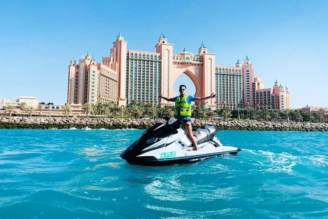 Man standing on a jet ski with arms raised in front of Atlantis The Palm hotel in Dubai Marina
