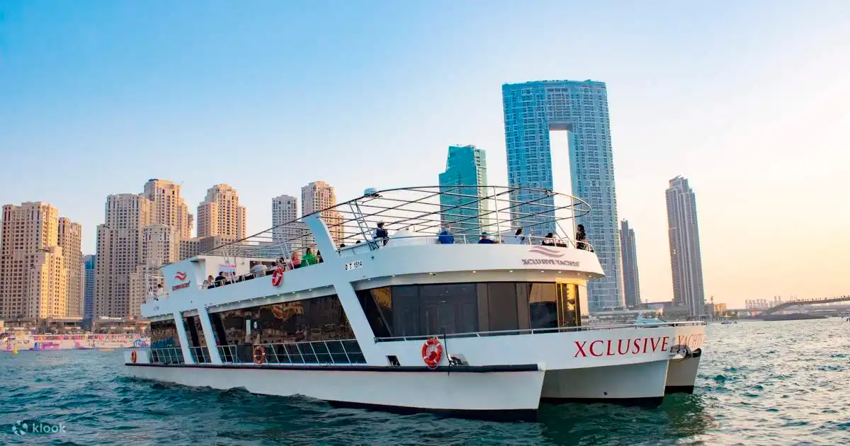 Modern white catamaran yacht cruising Dubai Marina at sunset with the city skyline in the background