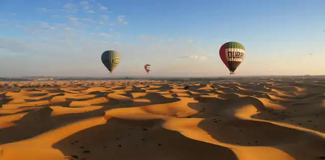 Multiple hot air balloons floating over golden rippled sand dunes in the Dubai desert at sunrise